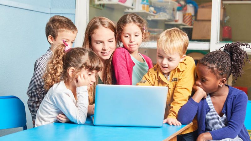 Pädagogin sitzt mit Kindern vor einem Laptop 